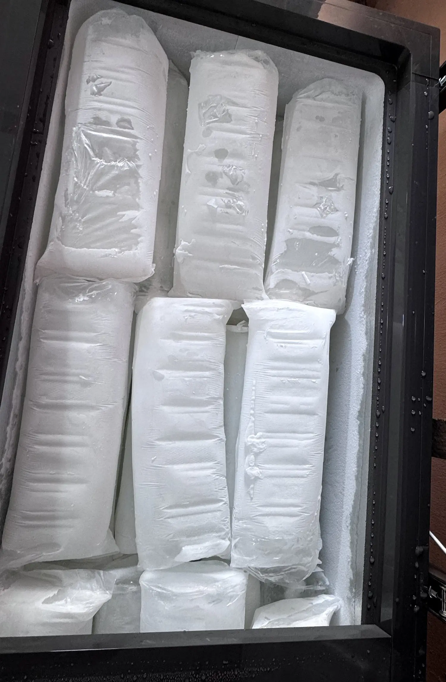 Rows of wrapped Boss Ice blocks standing in a chest freezer.